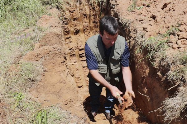 A man from Soils Inc. inside a dug hole in the soil examining soil samples under the trench