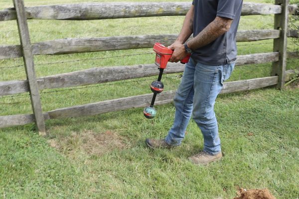 A professional from Soils Inc. walking in a grassy area with a device for line tracing for sewer and drain underground